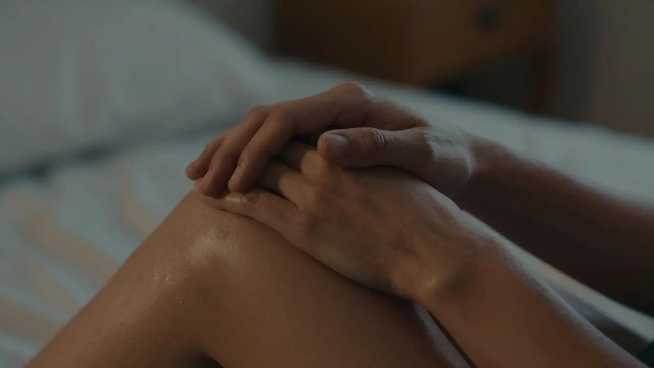 Dvě ruce se dotýkají na rameni, bez obličejů, v tichém prostředí večerního světla.